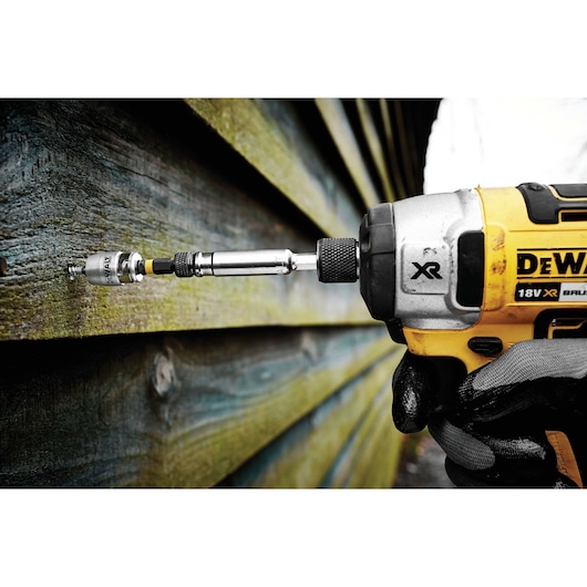 DEWALT drill with bit attached, in use on wooden siding outdoors, held by a gloved hand.