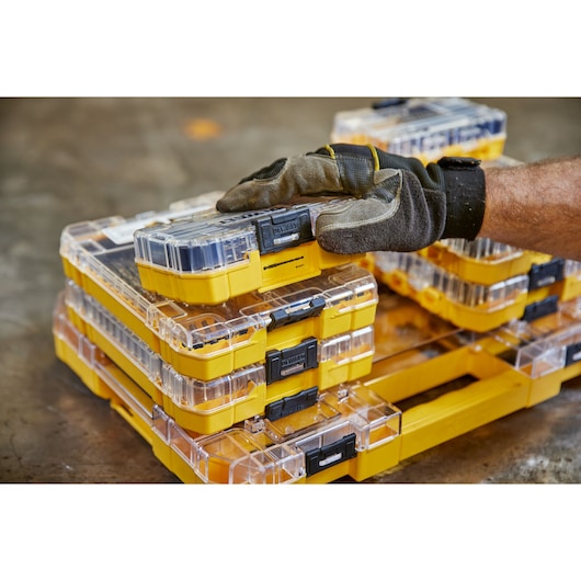 Gloved hand organizing stackable yellow DEWALT storage cases with clear lids on a workshop floor.