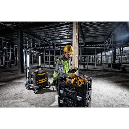 Worker in safety gear using DEWALT toolboxes at a construction site with metal framing and unfinished walls.