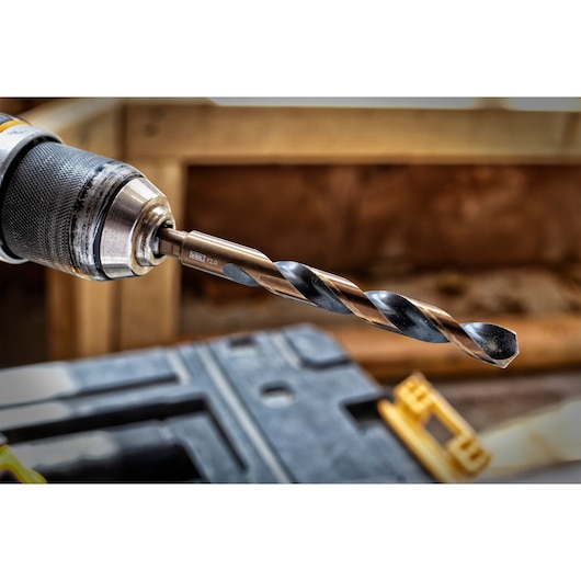 Close-up of a DEWALT drill bit attached to a power drill, shown in a workshop setting.