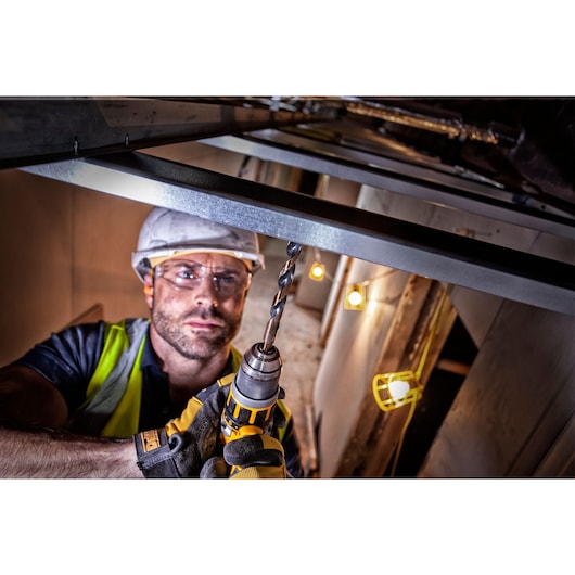 Worker using a DEWALT drill on metal at a construction site, wearing gloves and safety gear.