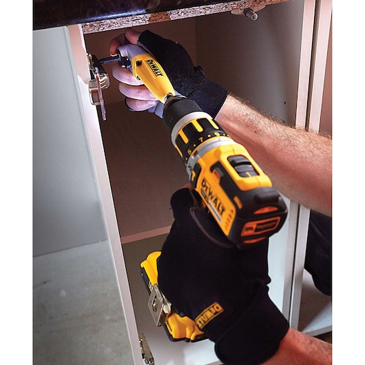 Person using a DEWALT drill inside a cabinet, wearing black gloves, assembling or fixing hinge hardware.
