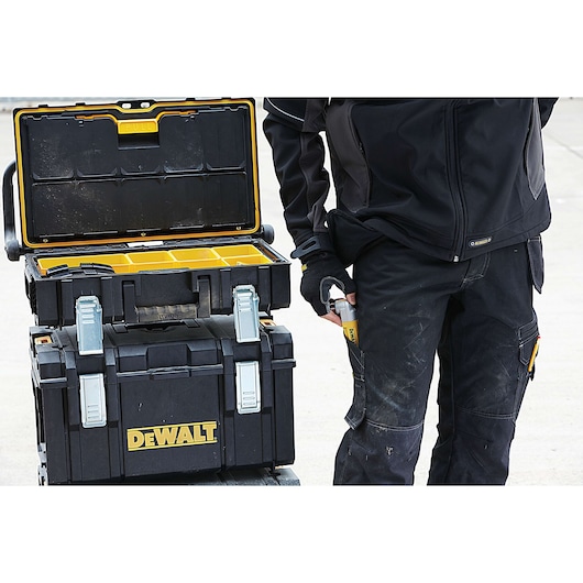 DEWALT toolboxes stacked with open compartments. A person in workwear stands nearby holding a tool.