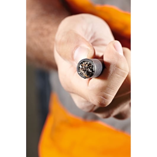 Hand holding a thick electrical cable with exposed copper wires. Safety vest visible in the background.