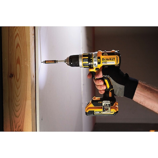 DEWALT cordless drill in use, drilling a screw into a wall, held by a gloved hand.