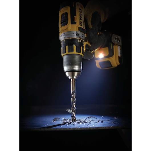 DEWALT cordless drill in use, drilling into metal with visible shavings and LED light illuminating the area.