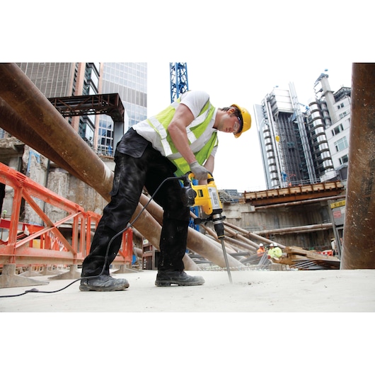 Worker uses DEWALT DT8088-QZ, DT8088 drill at a construction site, wearing safety gear. Photography category.