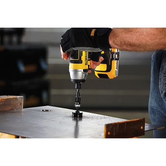 DEWALT drill in gloved hand drilling through metal sheet on workbench, close-up.