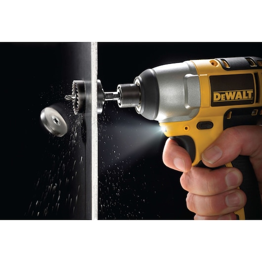 DEWALT drill with hole saw attachment cutting through metal, closeup of tool and hand in use.