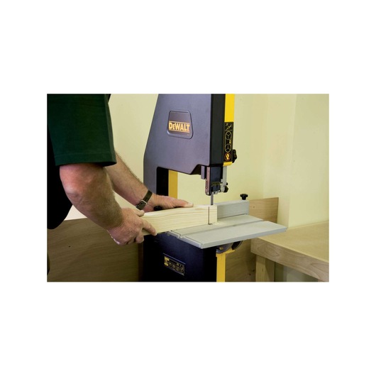 Person operating DEWALT bandsaw to cut wood in a workshop setting.