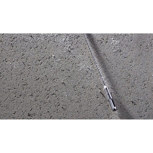 A DEWALT DT8909 long spiral drill bit is placed diagonally on a rough concrete surface.