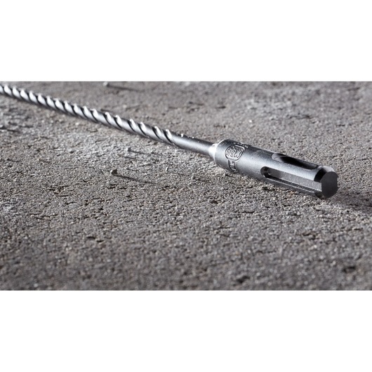 A DEWALT DT8910 masonry drill bit with a spiral design, lying on a rough concrete surface.
