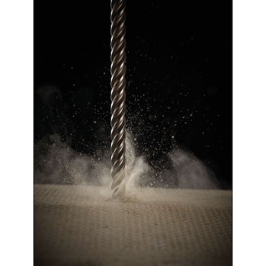 Metal drill bit drilling into a surface, dust and particles flying around, black background.