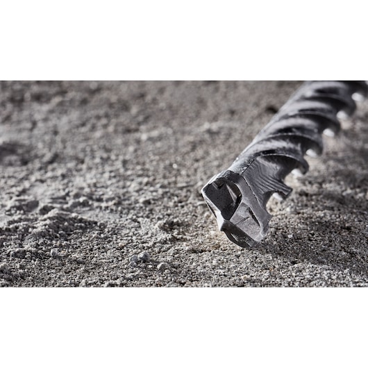 Close-up of a DEWALT DT8918 masonry drill bit lying on a gray, sandy surface, showing its pointed tip and spiral design.