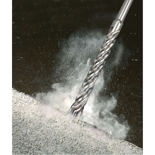 Close-up of a metal drill bit cutting into concrete, dust and particles flying around.