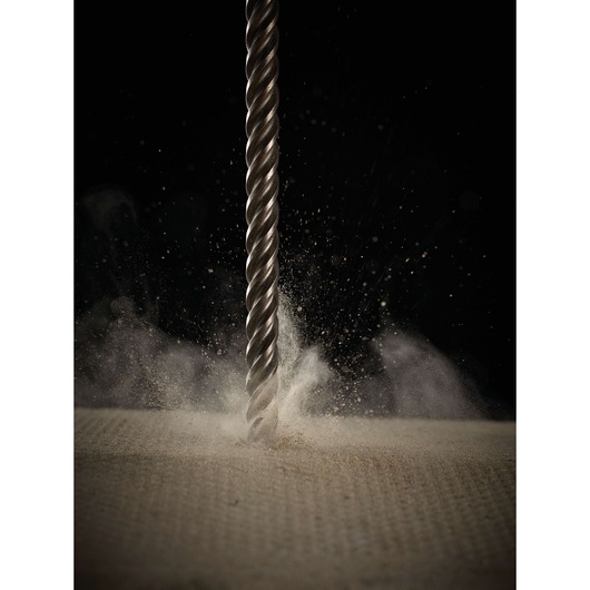 A DEWALT drill bit drilling into a surface, creating a burst of dust as it penetrates the material.
