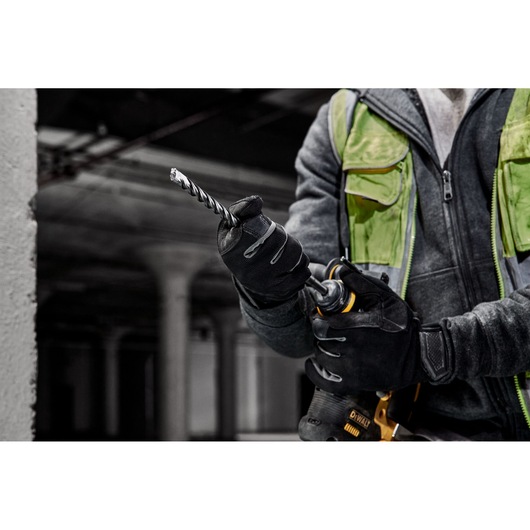 Gloved worker fits a DEWALT drill bit into a power drill in an industrial setting, wearing a green safety vest.