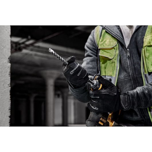 A person in gloves inserts a DEWALT drill bit into a power tool. Industrial background.