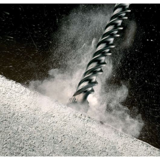 Close-up of a DEWALT drill bit cutting into concrete, with dust and debris flying.