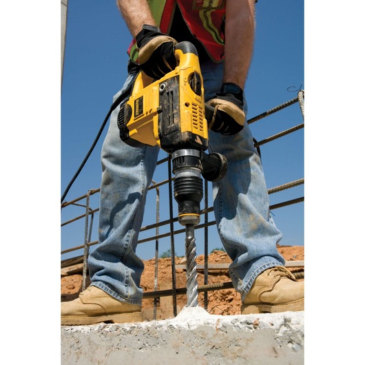 Person using a DEWALT electric drill to bore into concrete at a construction site.