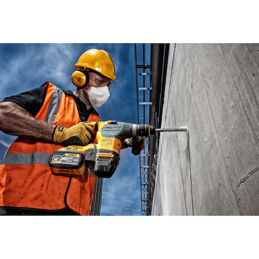 Worker in safety gear uses DEWALT cordless drill to bore into concrete wall outdoors.