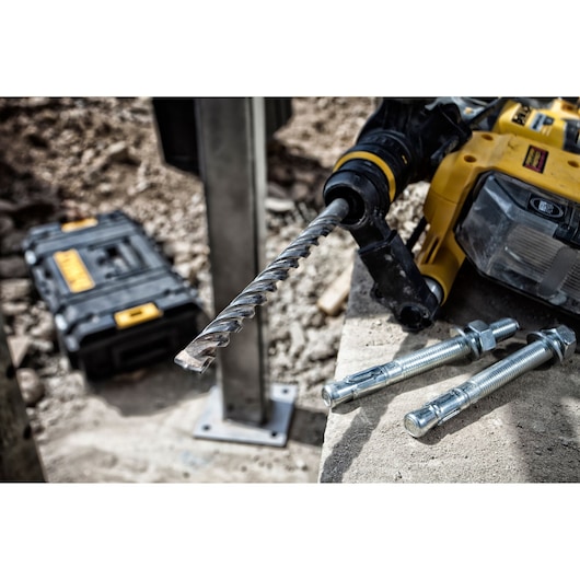 DEWALT drill with masonry bit and anchor bolts on concrete, tool case in background at a construction site.