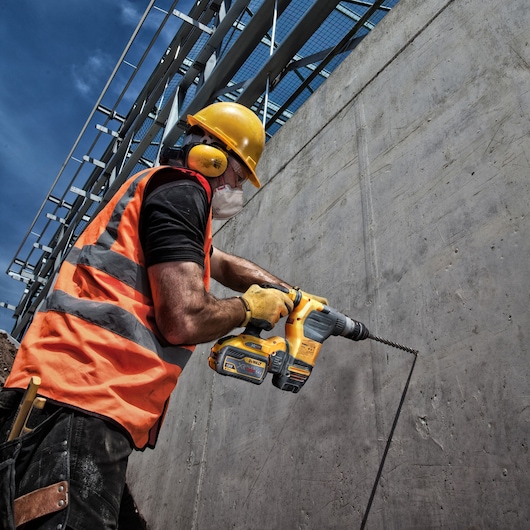 Worker using DEWALT DT9580, DT9580-QZ drill on concrete wall at construction site. Photography product.
