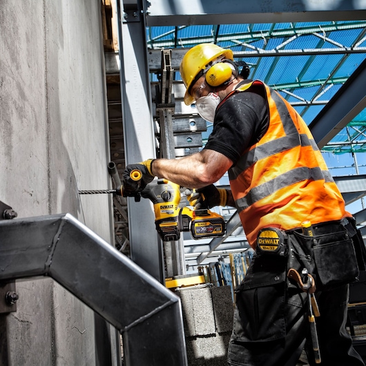 Worker uses DEWALT DT9580, DT9580-QZ drill at construction site, wearing safety gear.