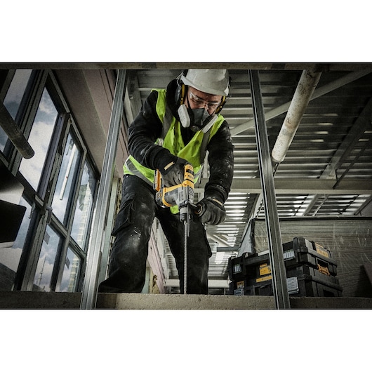 Worker uses DEWALT DT9621 drill at construction site, wearing safety gear and surrounded by DEWALT toolboxes.
