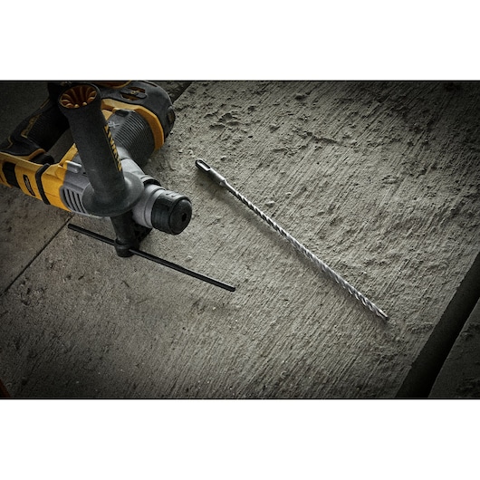 DEWALT drill and long masonry bit on a rough concrete surface, shown for construction or drilling work.