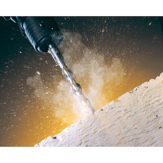 Close-up of a DEWALT drill bit making a hole in concrete, with dust and debris spraying out.