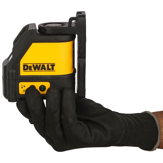 A person wearing a black work glove is holding a DEWALT DW088CG-XJ cross line laser level. The device is yellow and black and features the DEWALT logo and control buttons.