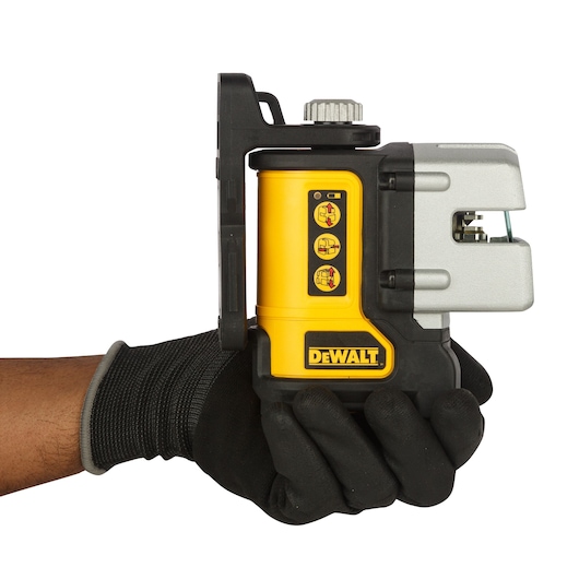 A DEWALT DW089K laser level tool held in a gloved hand, featuring a yellow and black body with control buttons and protective casing.