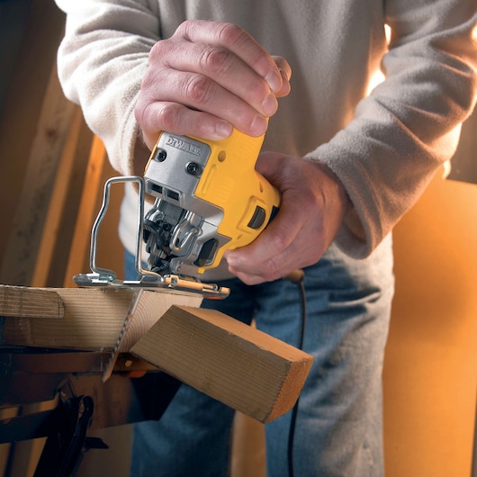 Person cutting wood with a yellow DEWALT jigsaw, close-up of hands and tool in action.