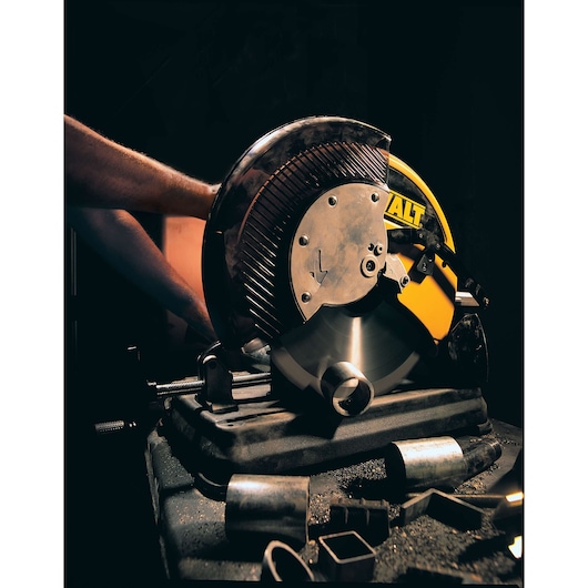 DEWALT DW872 cutting machine slicing metal pipes in a workshop, with scattered metal pieces on the surface.