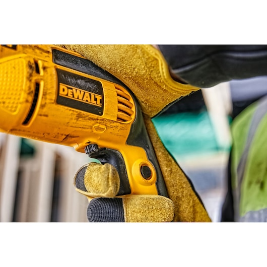 Close-up of a gloved hand holding a DEWALT electric drill at a construction site.