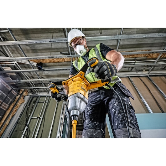 Person using DEWALT DWD241 mixer drill at a construction site, wearing safety gear and gloves.
