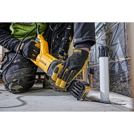 Person uses DEWALT reciprocating saw to cut pipe on construction site, wearing gloves and kneepads.