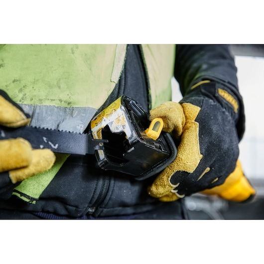 Gloved hands attach a DEWALT tool to a belt, showing close-up of work gear and rugged gloves.