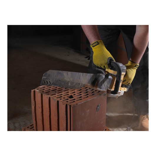 Person cuts a brick with a DEWALT power saw, wearing yellow gloves, in a construction setting.