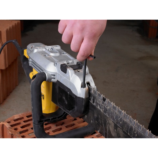 Hand adjusts DEWALT saw blade with a tool. Saw is placed on a brick, used for construction or masonry tasks.