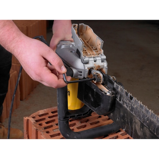 Person uses a hex key to adjust a DEWALT brick saw on a construction site.