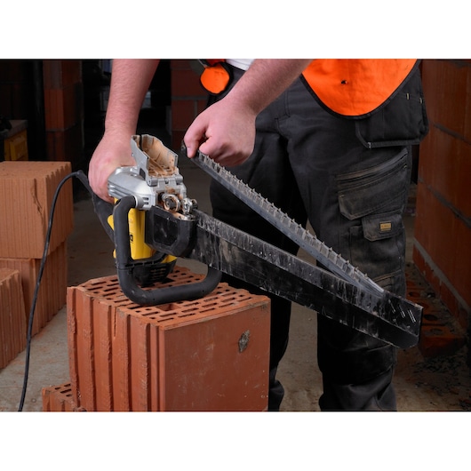 Person uses a DEWALT electric saw to cut construction bricks on a worksite.