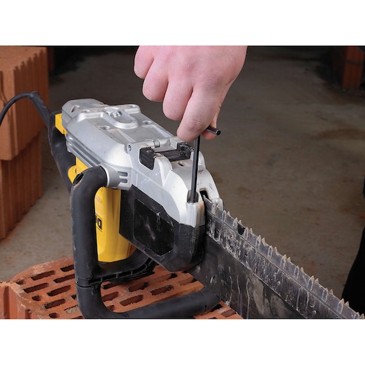 Hand uses tool to adjust blade on a DEWALT power saw placed on a brick.