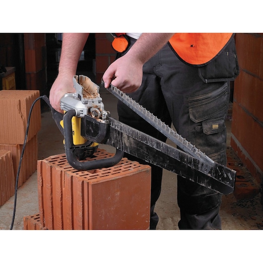 Person uses a DEWALT electric saw to cut masonry blocks. Safety vest and work pants are visible.