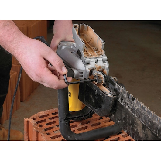 Person adjusts a DEWALT electric brick saw with a hex key, placed on a brick surface for maintenance.
