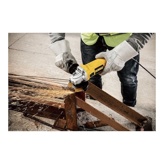 A person wearing safety gloves and a vest is using a yellow DEWALT angle grinder (model DWE4117) to cut through a metal beam, creating sparks.