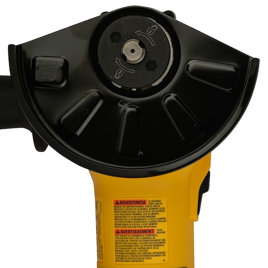 Close-up of a DEWALT angle grinder head with guard and warning label on yellow housing.