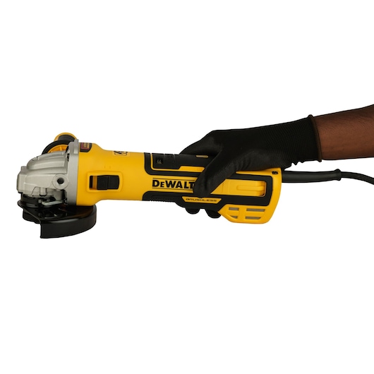 A person wearing a black glove is holding a yellow and black DEWALT angle grinder with a cord.
