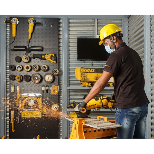 Person uses a DEWALT power tool to cut metal, with sparks flying. Tools and accessories are organized in the background.